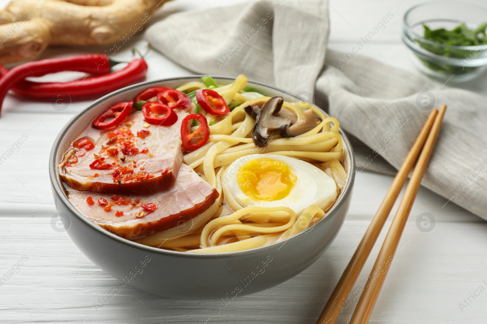 Photo of Delicious ramen in bowl and chopsticks on white wooden table. Noodle soup