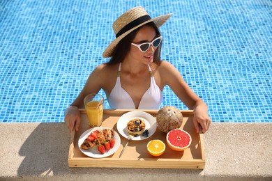 Young woman with delicious breakfast on tray in swimming pool