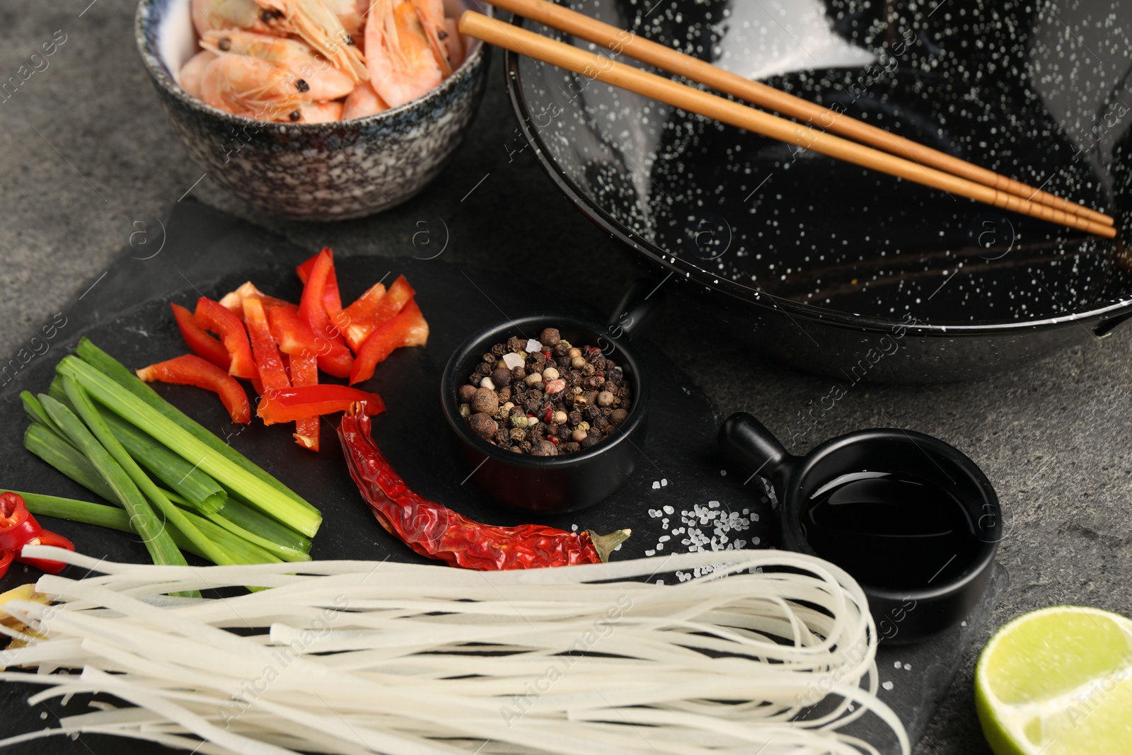 Photo of Different products and wok with chopsticks on dark table, closeup