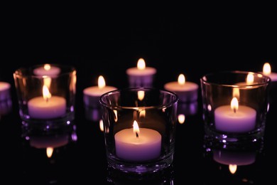 Image of Beautiful burning violet wax candles on black background. Funeral attributes