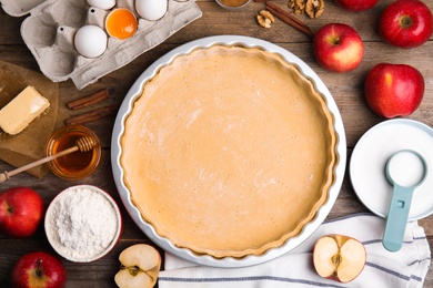 Photo of Raw dough and ingredients for traditional English apple pie on wooden table, flat lay