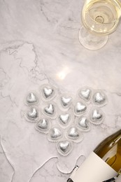 Heart made with delicious chocolate candies and champagne on white marble table, flat lay