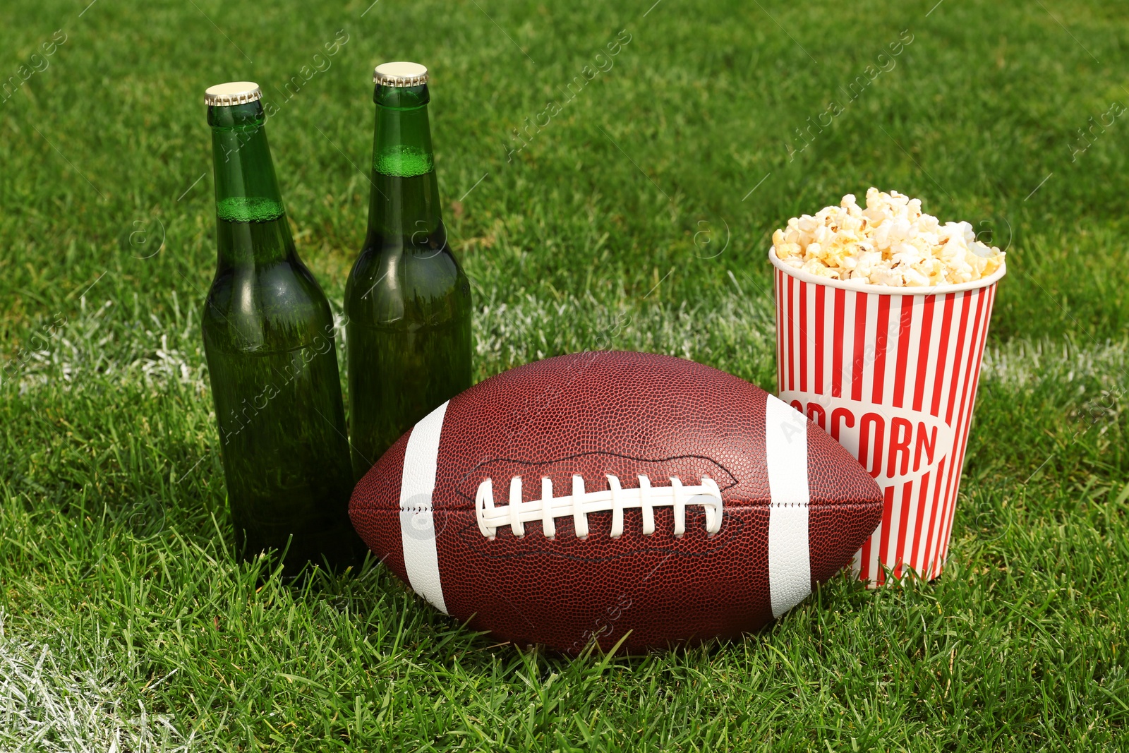 Photo of American football ball with beer and popcorn on green field grass