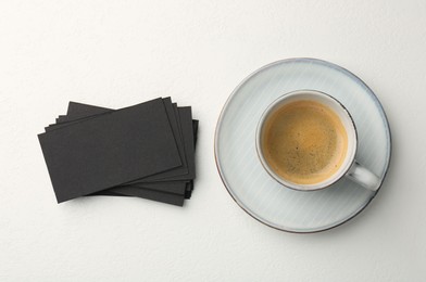 Photo of Blank black business cards and cup of coffee on white table, top view. Mockup for design