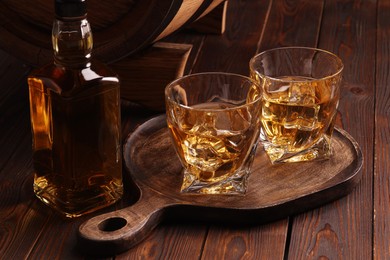 Whiskey with ice cubes in glasses and bottle on wooden table