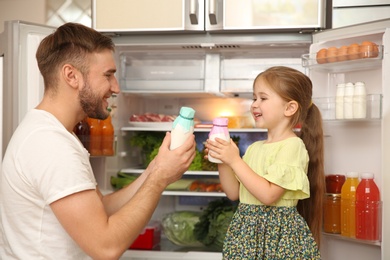 Young father and daughter with yogurt bottles near refrigerator at home