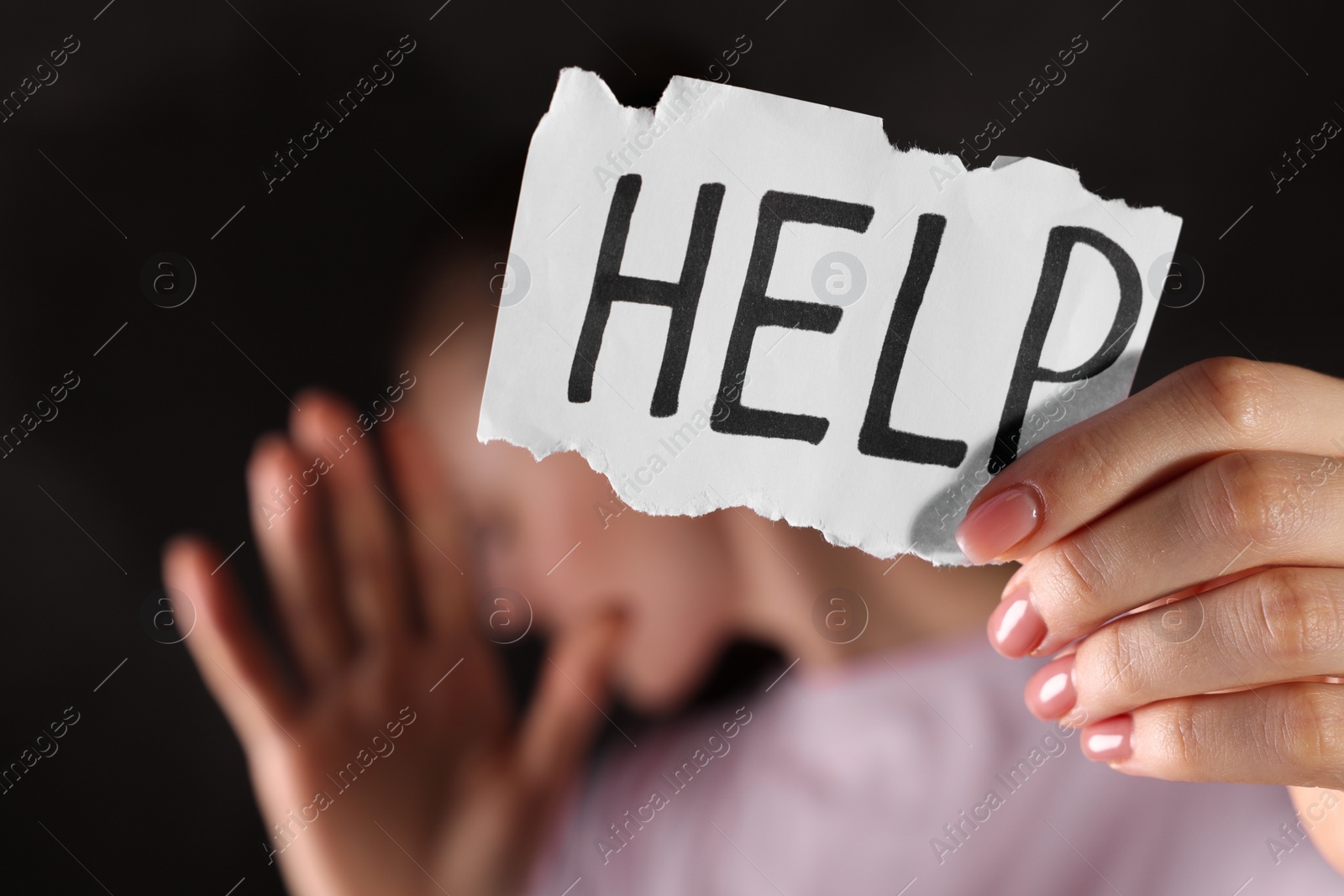 Photo of Woman holding piece of paper with word Help on dark background, closeup. Domestic violence concept