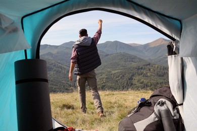 Man in mountains on sunny day, view from camping tent