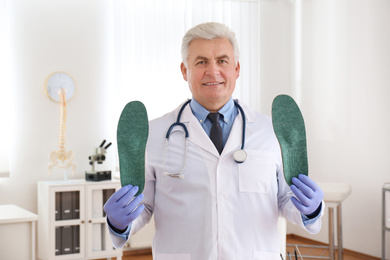 Senior male orthopedist showing insoles in clinic
