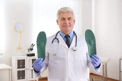 Photo of Senior male orthopedist showing insoles in clinic