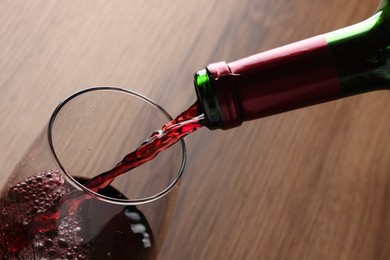 Photo of Pouring tasty red wine in glass at wooden table, closeup