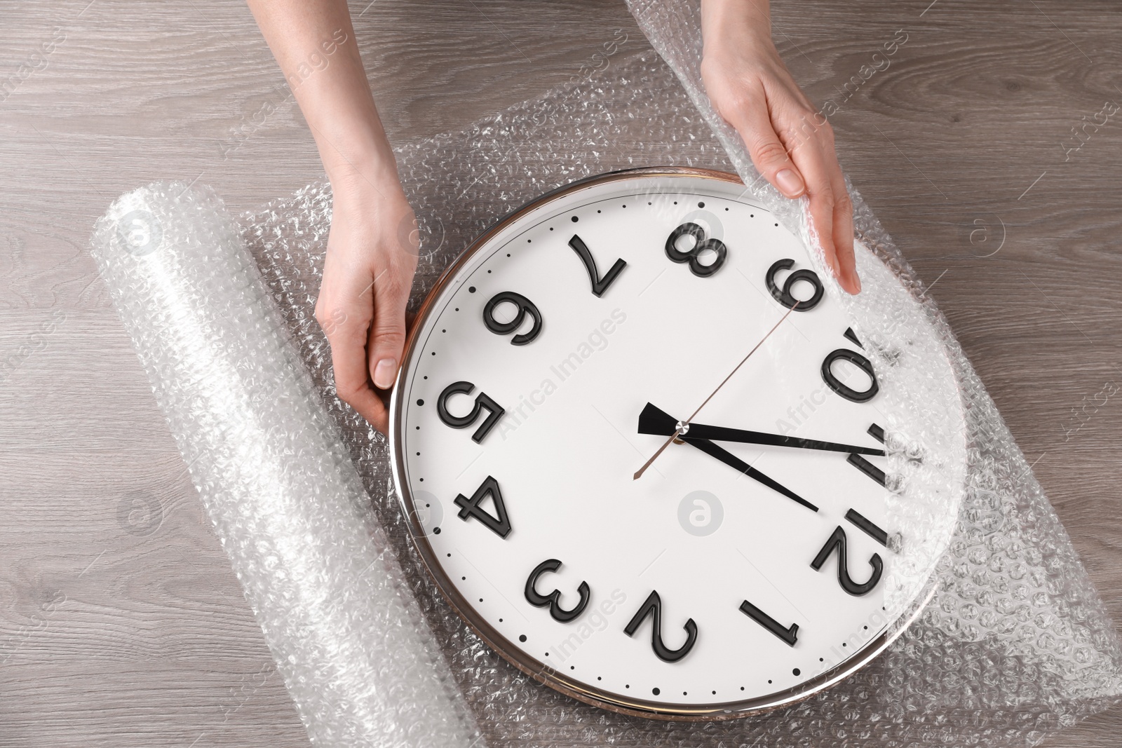 Photo of Woman covering wall clock with bubble wrap at wooden table, closeup