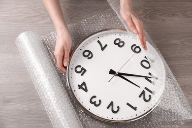 Photo of Woman covering wall clock with bubble wrap at wooden table, closeup