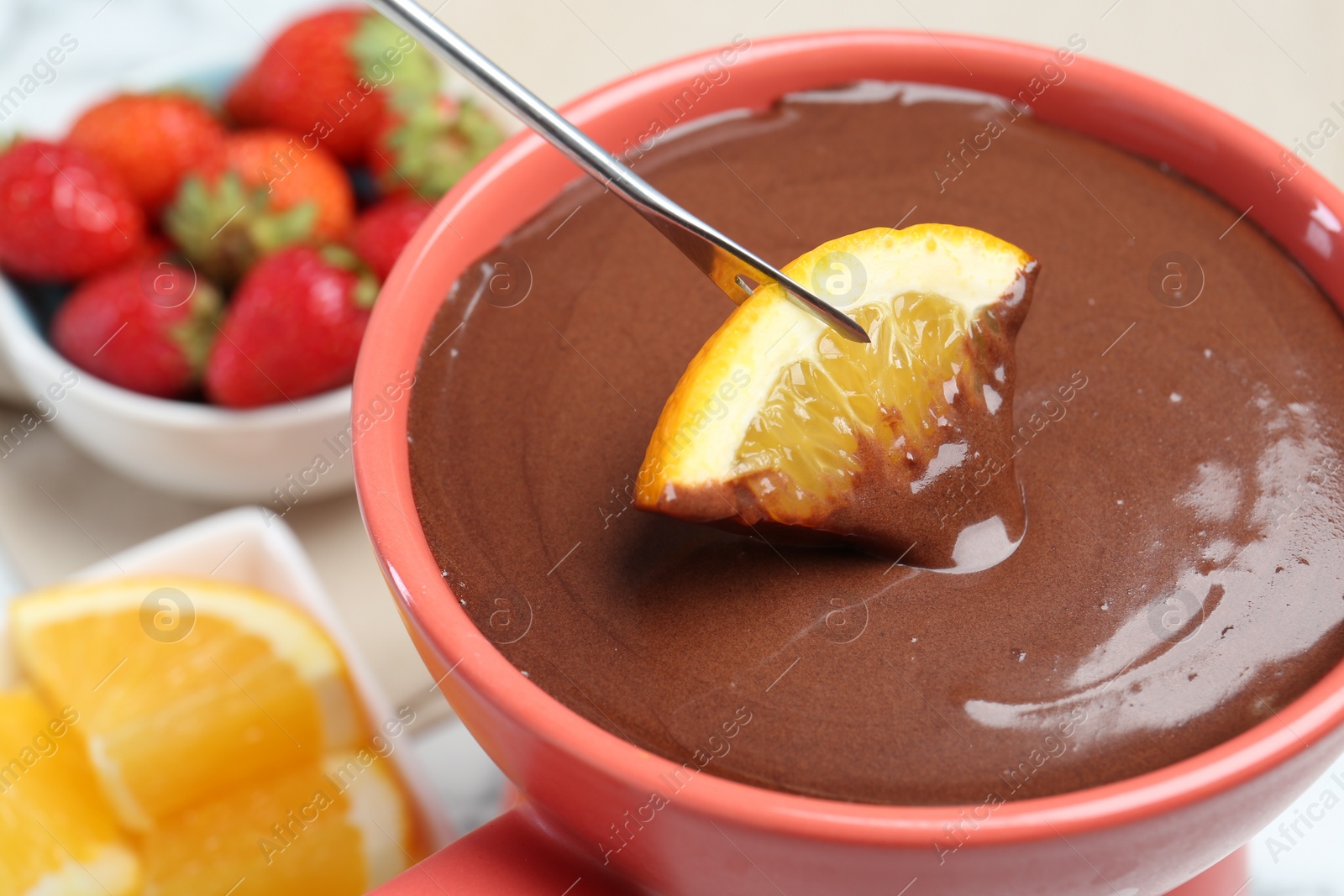 Photo of Dipping fresh orange into fondue pot with melted chocolate at table, closeup