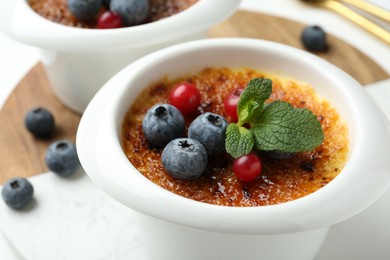 Photo of Delicious creme brulee with berries and mint in bowls on table, closeup