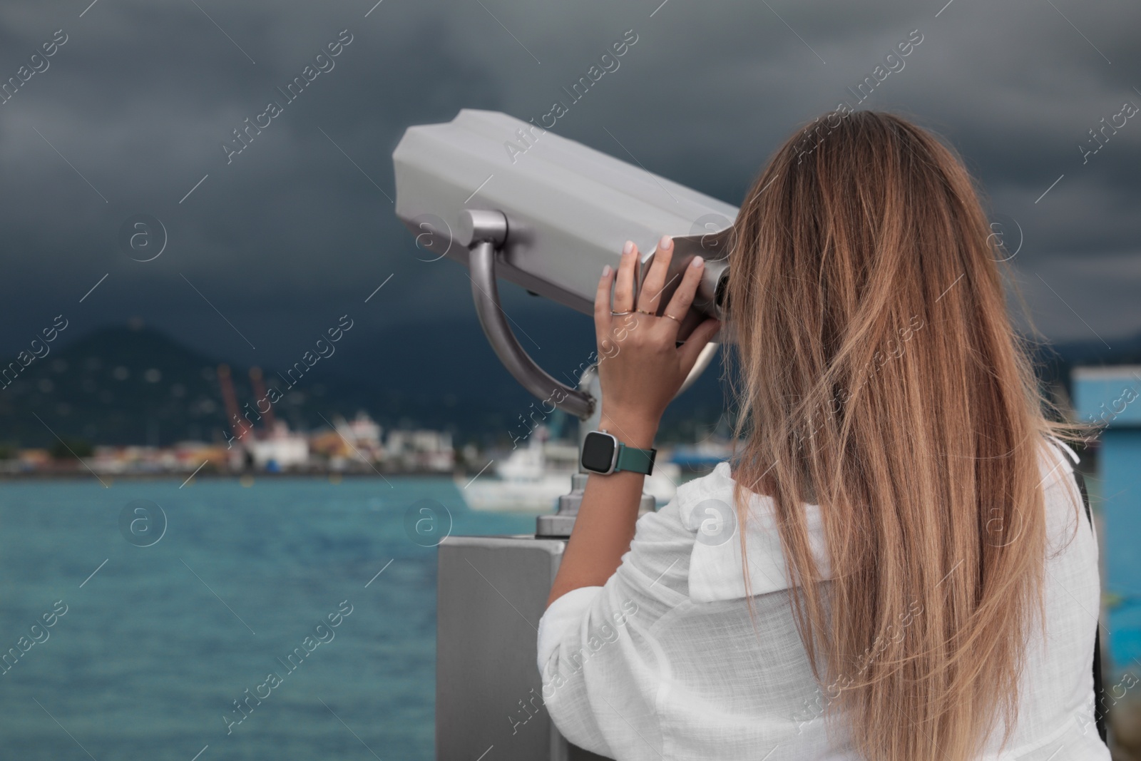 Photo of Woman looking through mounted binoculars at mountains. Space for text