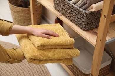 Woman putting towels into storage basket indoors, closeup