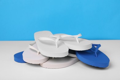 Photo of Many different flip flops on white table against light blue background