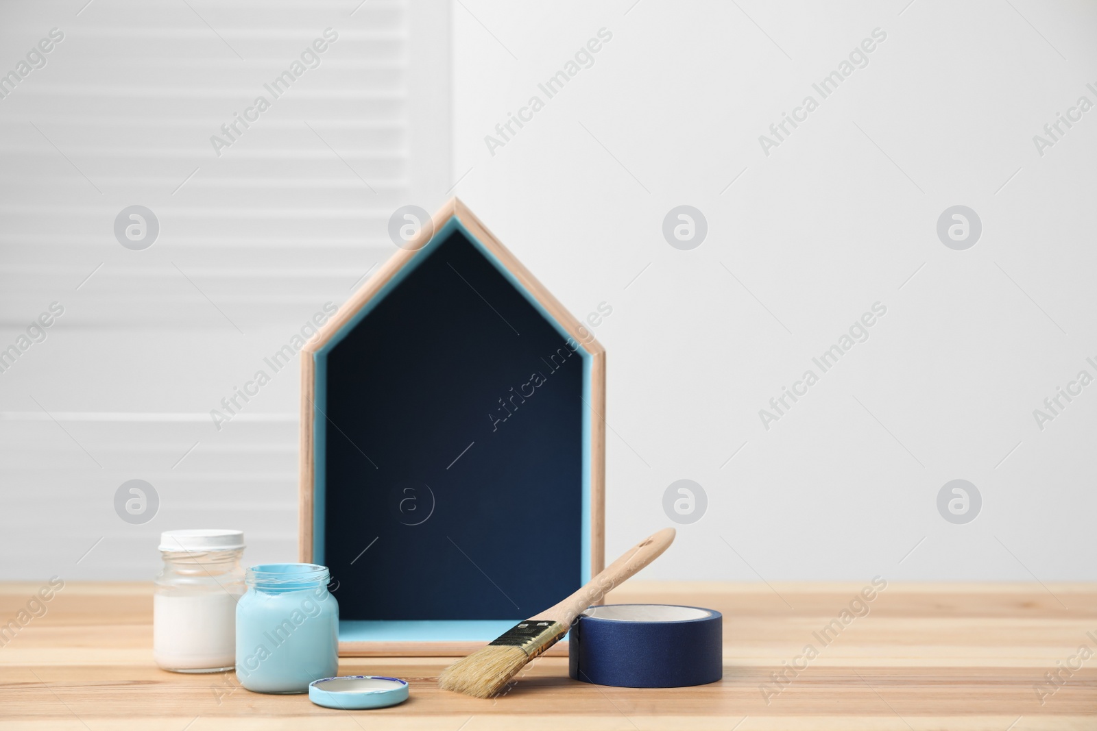 Photo of House shaped shelf, jars of paints and decorator tools on table. Space for text