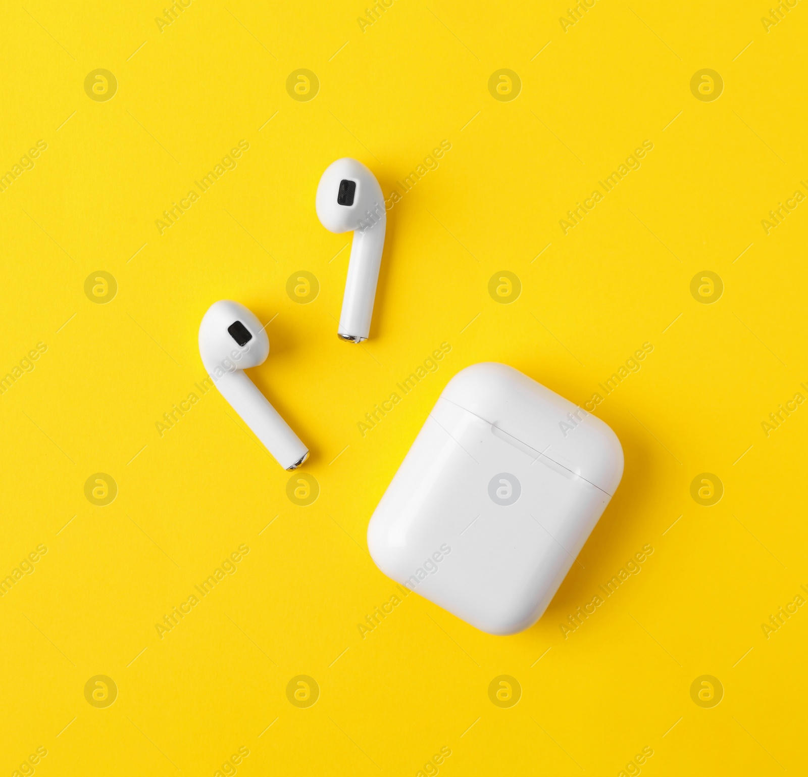 Photo of Modern wireless earphones and charging case on yellow background, flat lay