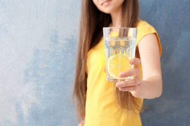 Young woman holding glass of lemon water on color background, closeup