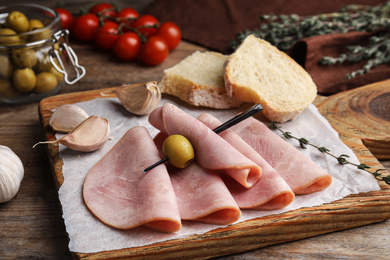 Photo of Slices of tasty ham with olive on wooden table