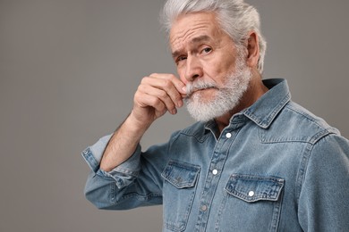 Photo of Senior man touching mustache on grey background, space for text