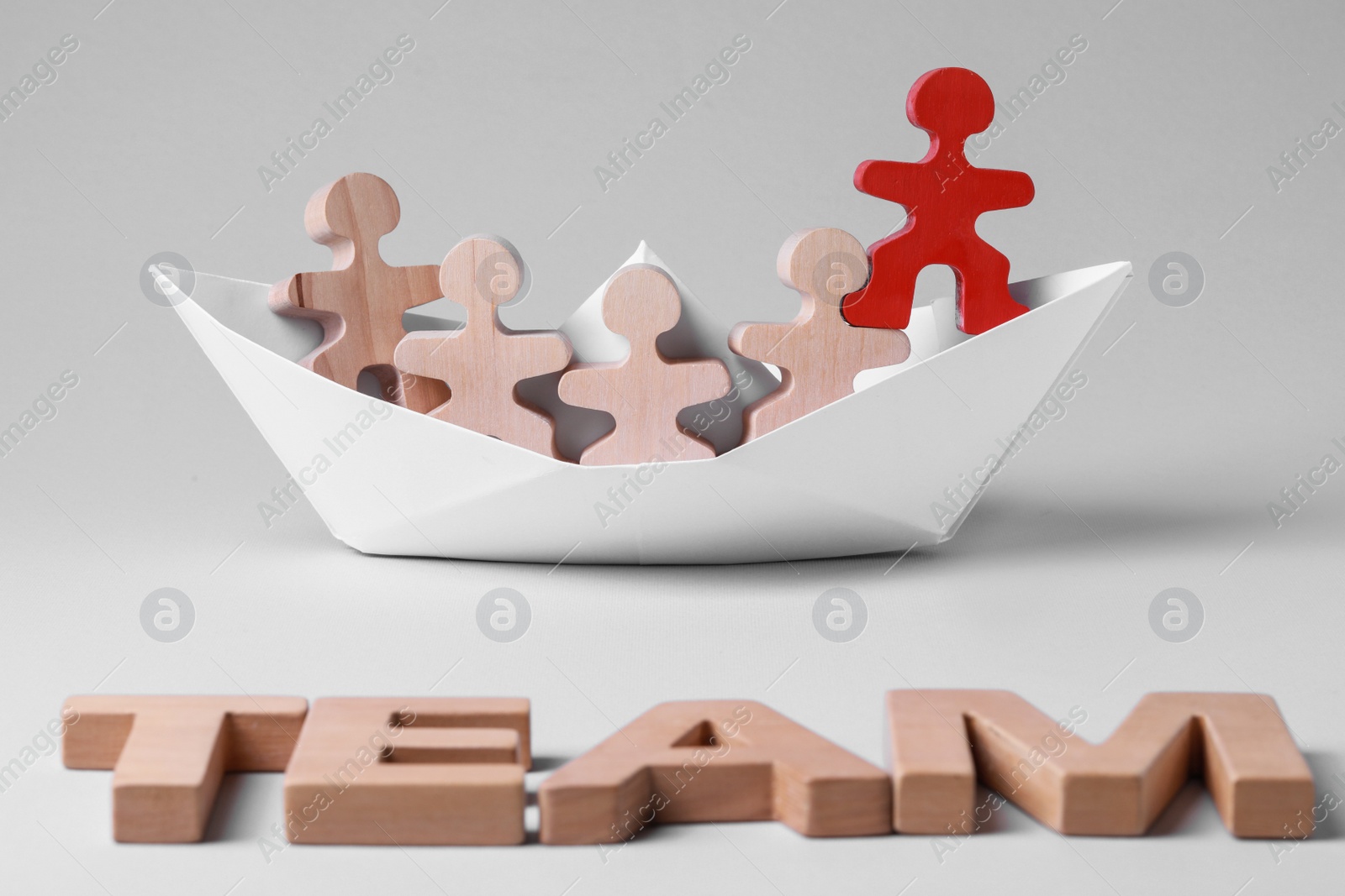 Photo of Red figure among wooden ones in paper boat and word Team on white background. Recruiter searching employee