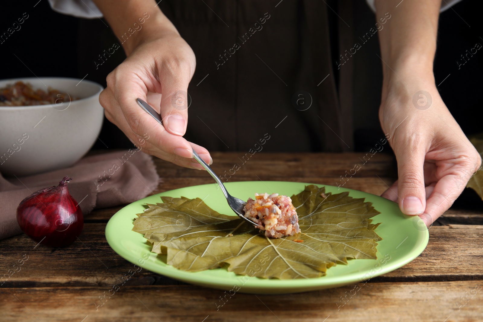 Photo of Woman preparing stuffed grape leaves at wooden table, closeup