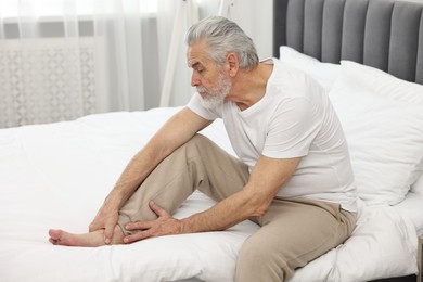 Photo of Arthritis symptoms. Man suffering from pain in leg on bed at home