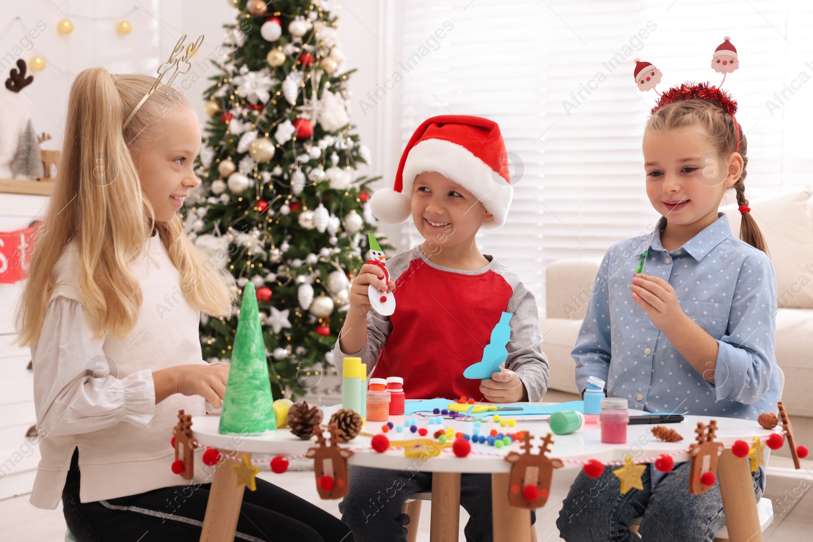 Photo of Cute little children making Christmas crafts at table in decorated room