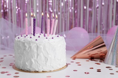 Photo of Delicious cake with burning candles and party hats on white table. Space for text