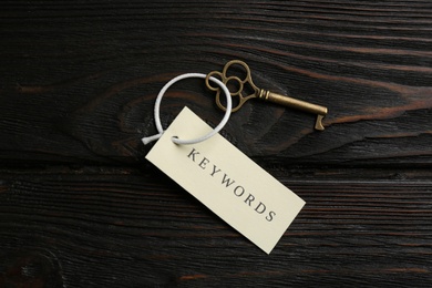 Photo of Key with tag KEYWORDS on wooden background, top view