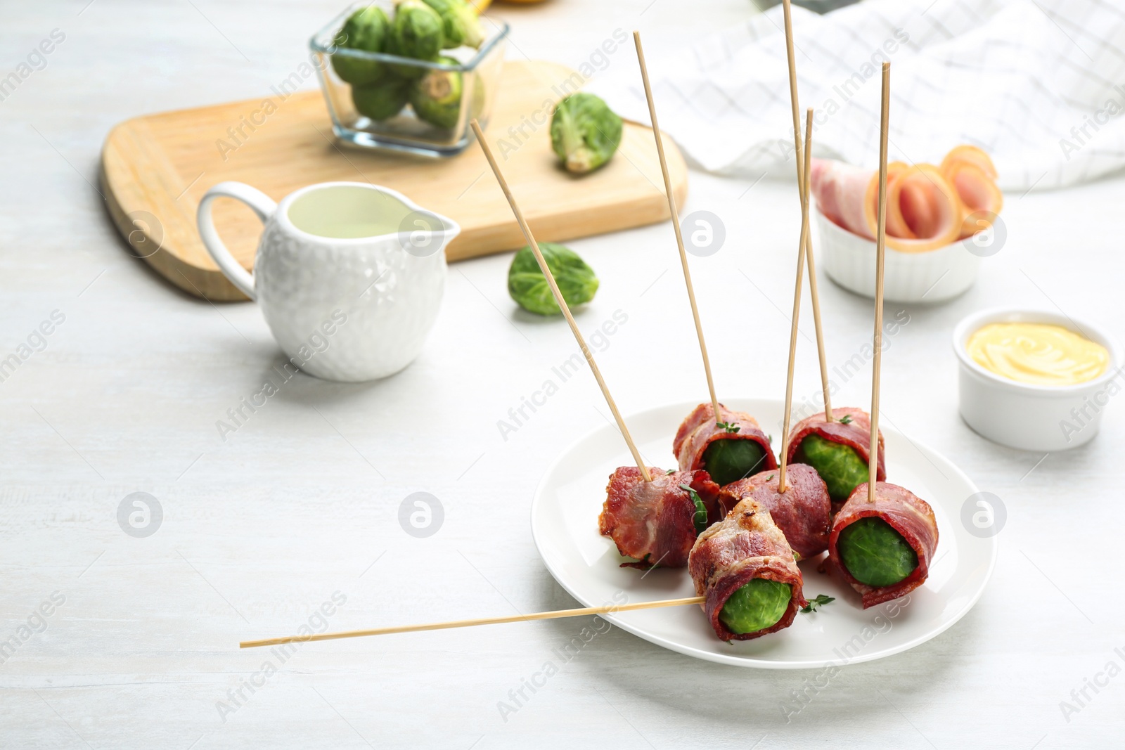 Photo of Brussels sprouts wrapped in bacon served on white table