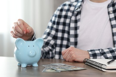 Photo of Financial savings. Man putting coin into piggy bank at wooden table, closeup