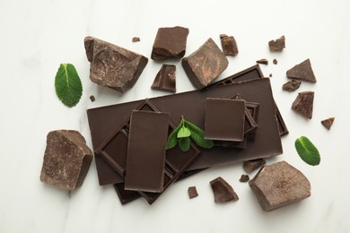 Photo of Tasty dark chocolate pieces with mint on white table, flat lay