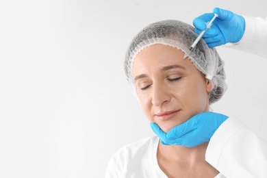 Mature woman getting facial injection and space for text on white background. Cosmetic surgery concept