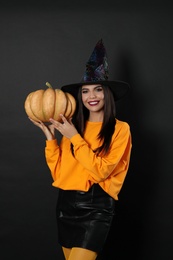 Photo of Beautiful woman wearing witch costume with pumpkin for Halloween party on black background