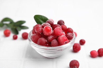 Frozen red cranberries in bowl and green leaves on white tiled table, closeup
