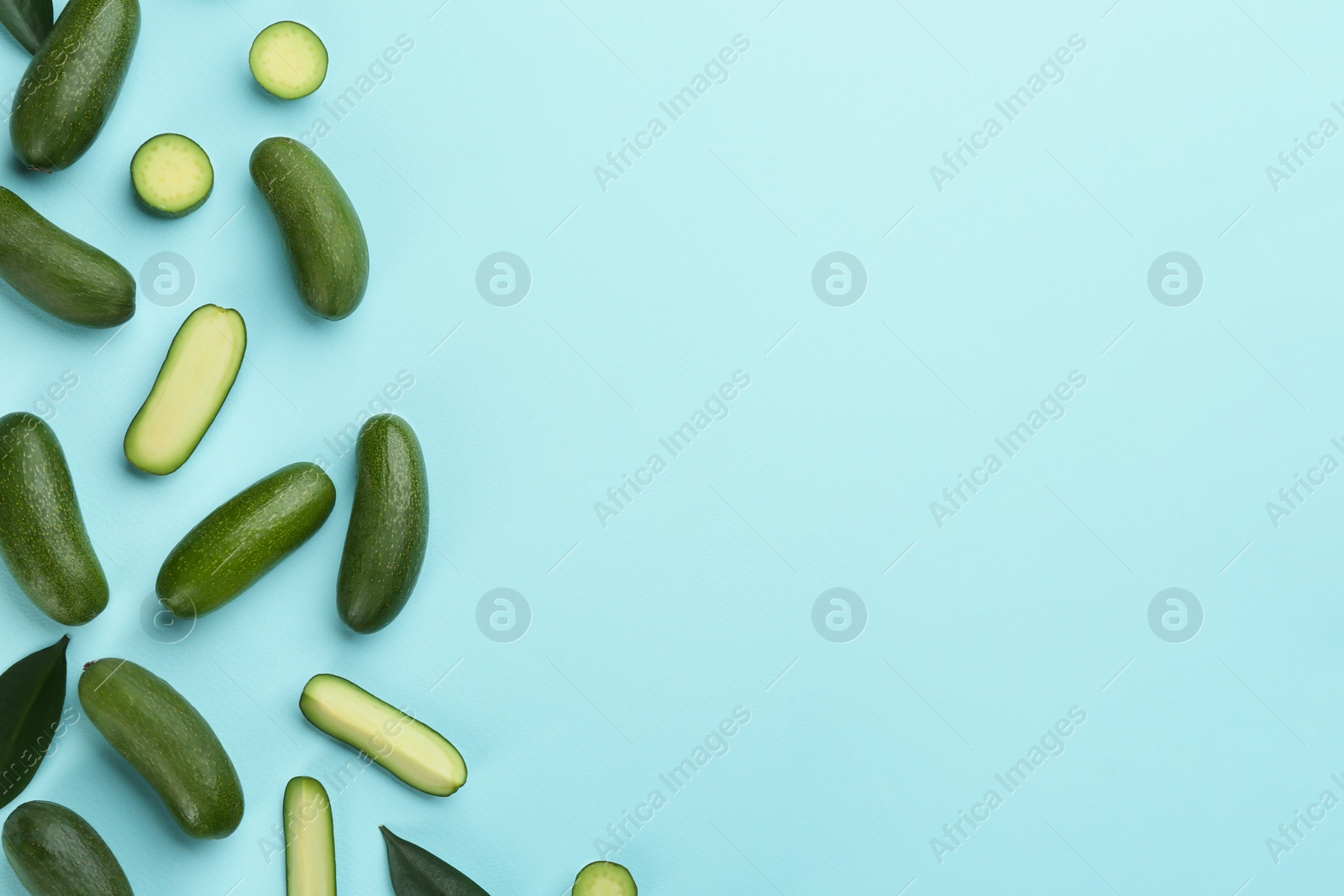 Photo of Whole and cut seedless avocados with green leaves on light blue background, flat lay. Space for text