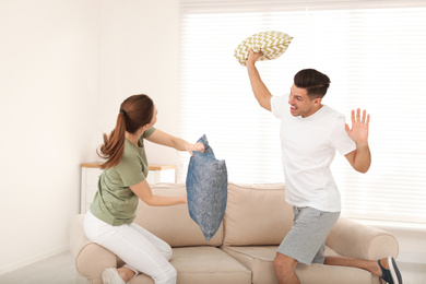 Photo of Happy couple having pillow fight in living room