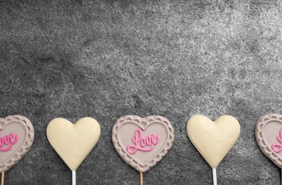 Photo of Different chocolate heart shaped lollipops on grey table, flat lay. Space for text