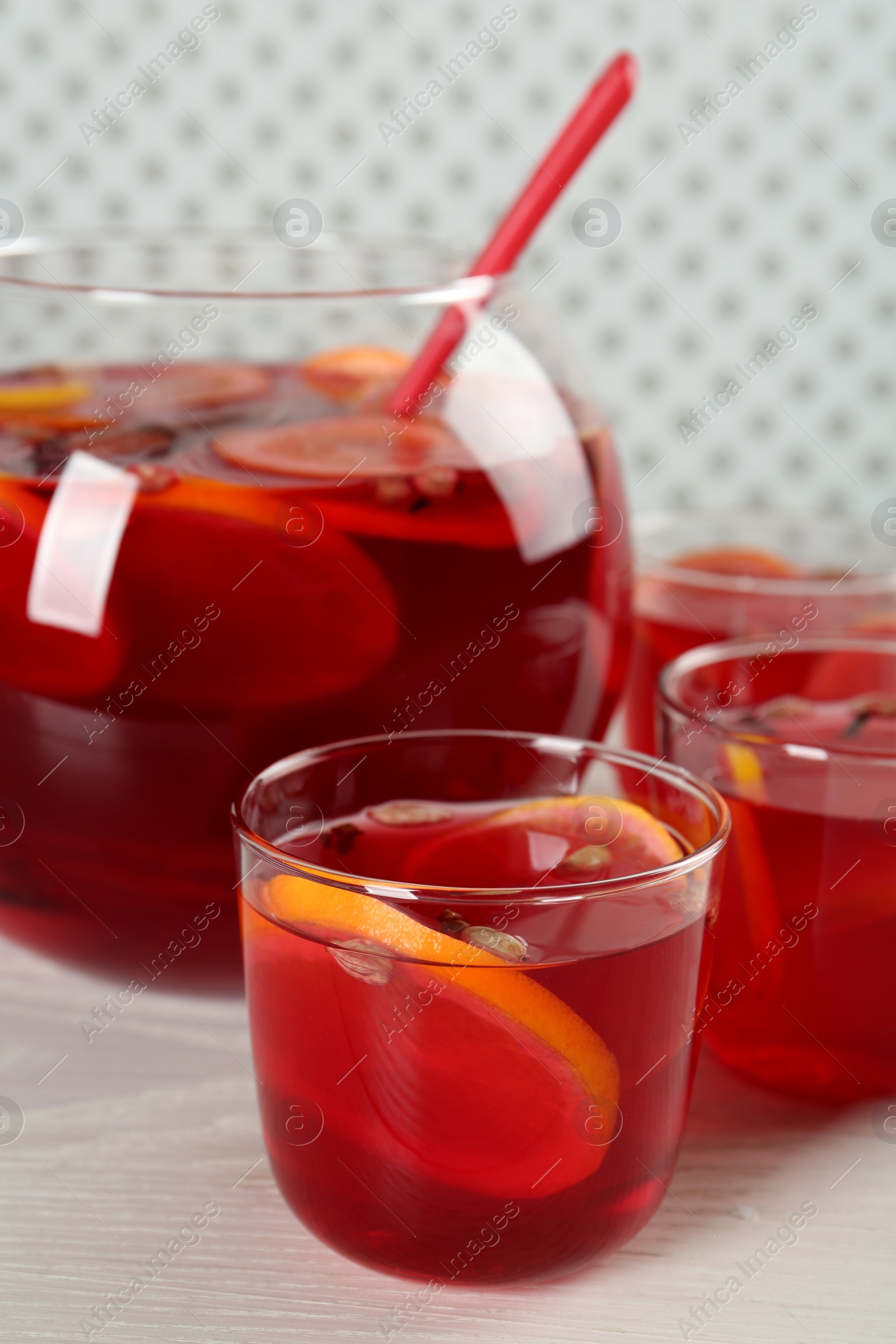 Photo of Glasses and bowl of delicious aromatic punch drink on white wooden table, closeup