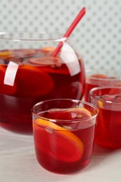 Glasses and bowl of delicious aromatic punch drink on white wooden table, closeup