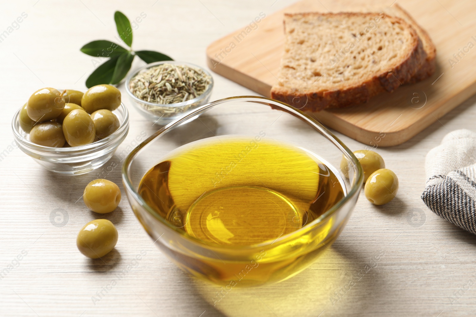 Photo of Glass bowl with fresh olive oil on white wooden table