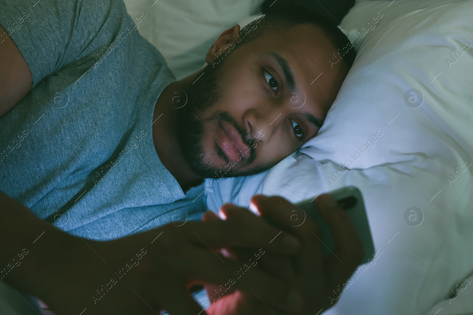 Photo of Young man using smartphone in bed at night. Internet addiction