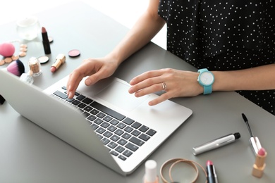 Photo of Young woman with makeup products using laptop at table. Beauty blogger