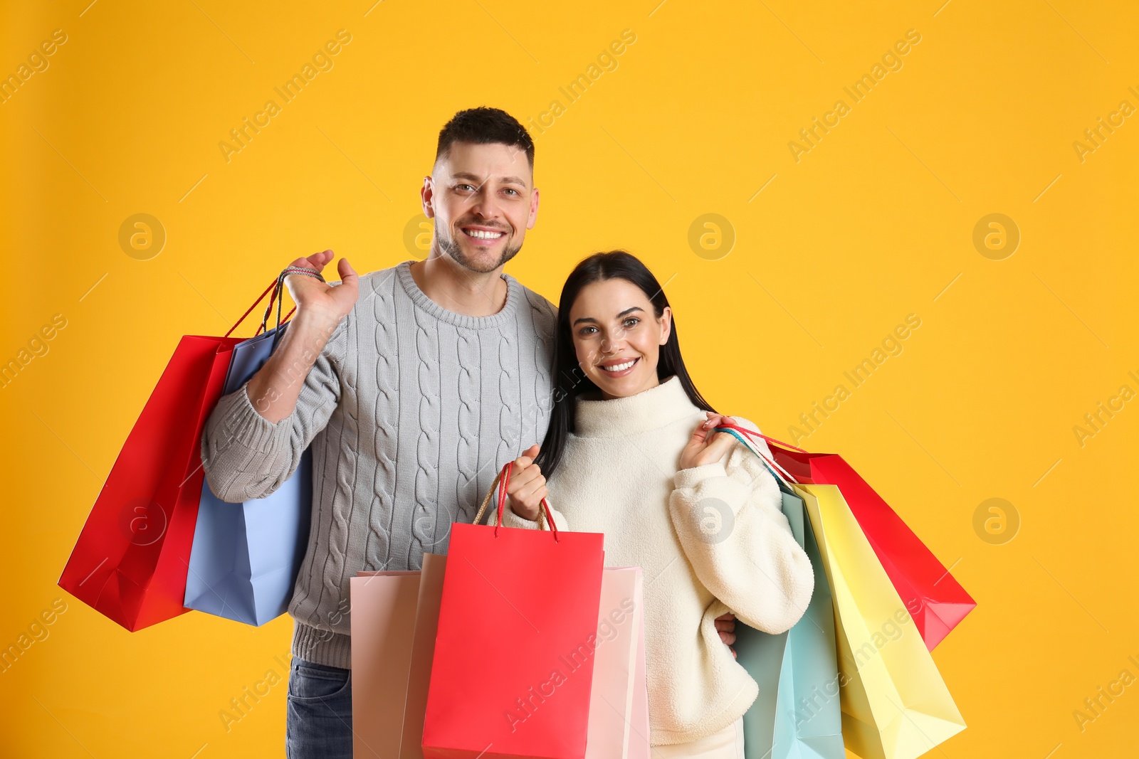 Photo of Happy couple with paper bags on yellow background. Christmas shopping