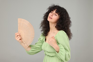 Woman with hand fan suffering from heat on light grey background