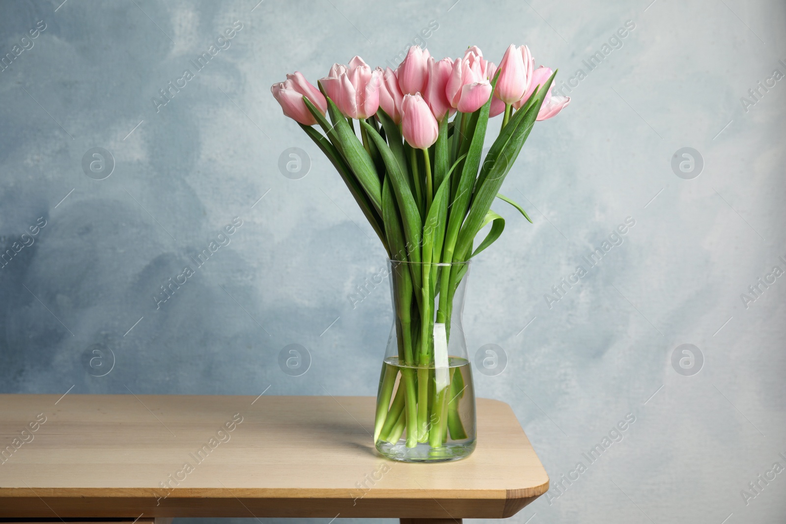 Photo of Beautiful pink spring tulips in vase on wooden table